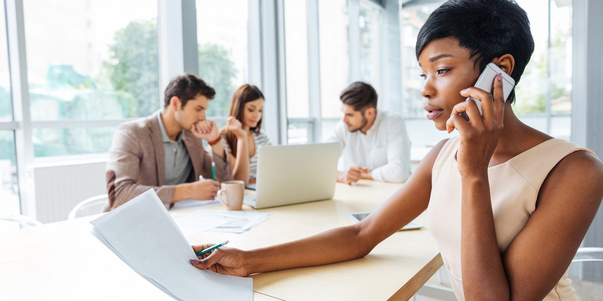 Serious businesswoman with documents talking on cell phone in office