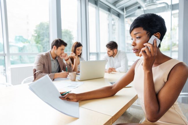 Serious businesswoman with documents talking on cell phone in office